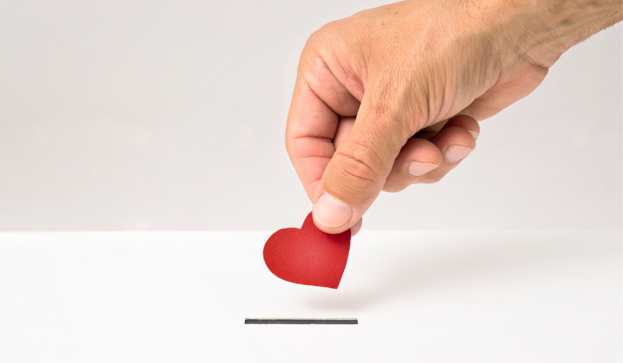 A hand holding a red paper heart and placing it into a slot in a box